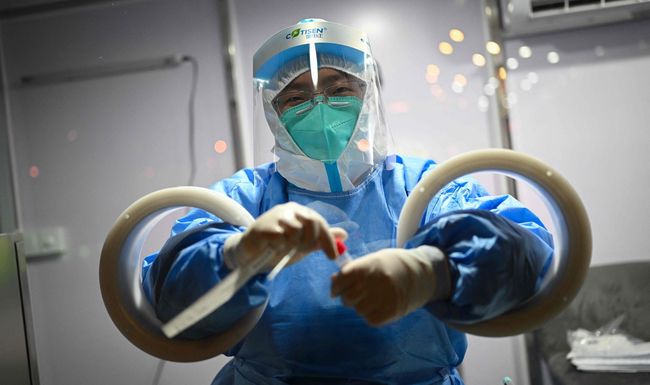 TOPSHOT - An employee, wearing a hazmat suit, holds a swab sample just collected during a daily Covid-19 pcr test on a member of the media ahead of the 2022 Winter Olympics in Beijing on January 27, 2022. (Photo by Fabrice COFFRINI / AFP)