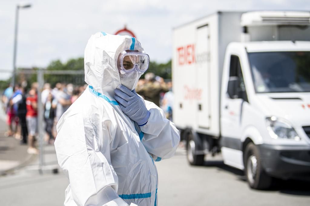 Ein Bundeswehr-Soldat im Schutzanzug und mit Mund-Nasenschutzmaske steht vor einem Bauzaun, hinter dem Menschen stehen, die sich in Quarantäne befinden.