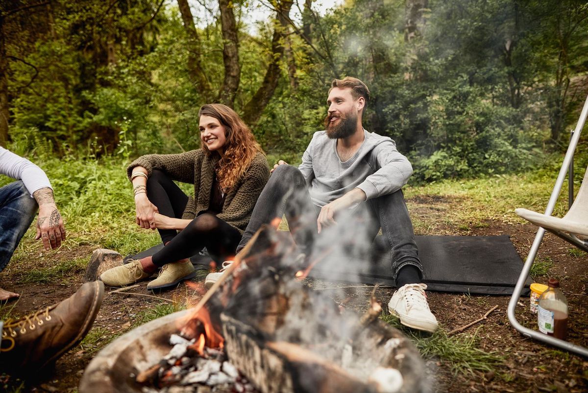 Ein Mann und eine Frau machen zusammen mit Freunden in der Natur ein Feuer. 