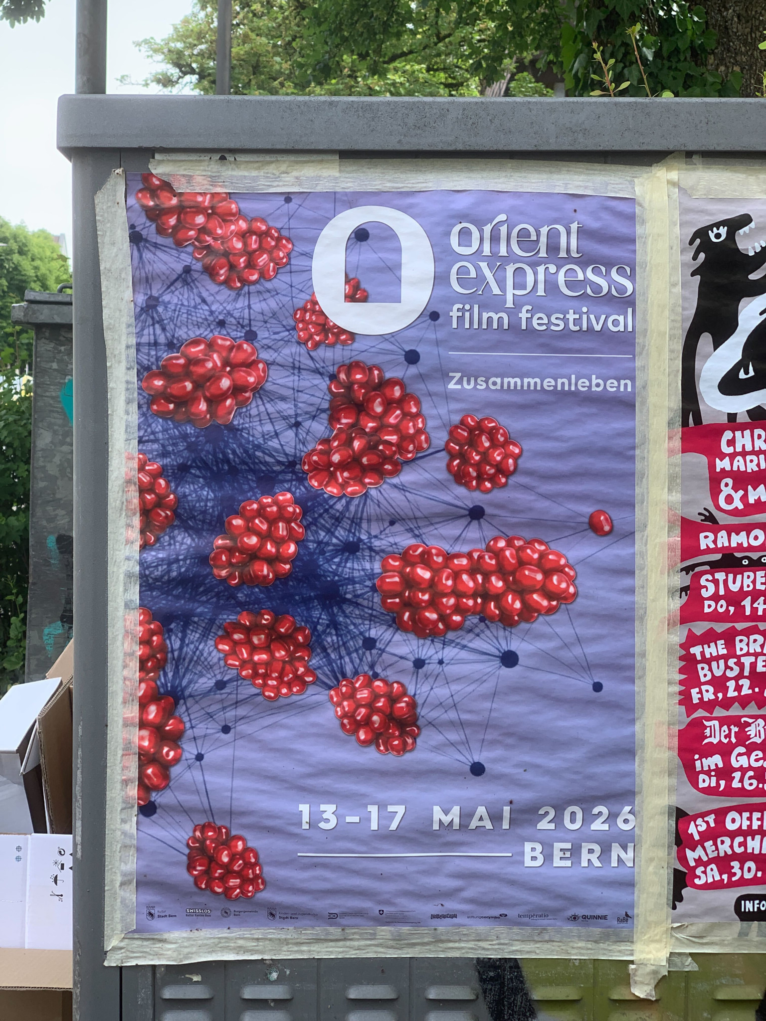 Plakat des Orient Express Film Festivals in Bern, 13.–17. Mai 2026, mit dem Motto «Zusammenleben» und roten Kugeln auf blauem Netz-Hintergrund.