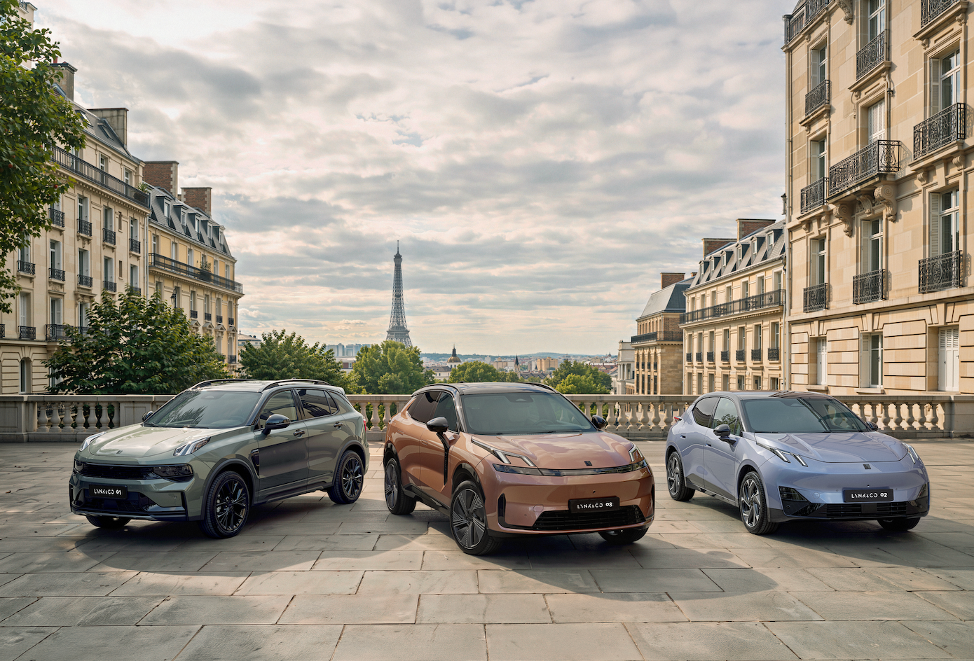 Drei Lynk & Co Elektroautos in Grau, Braun und Lila vor dem Eiffelturm in Paris.