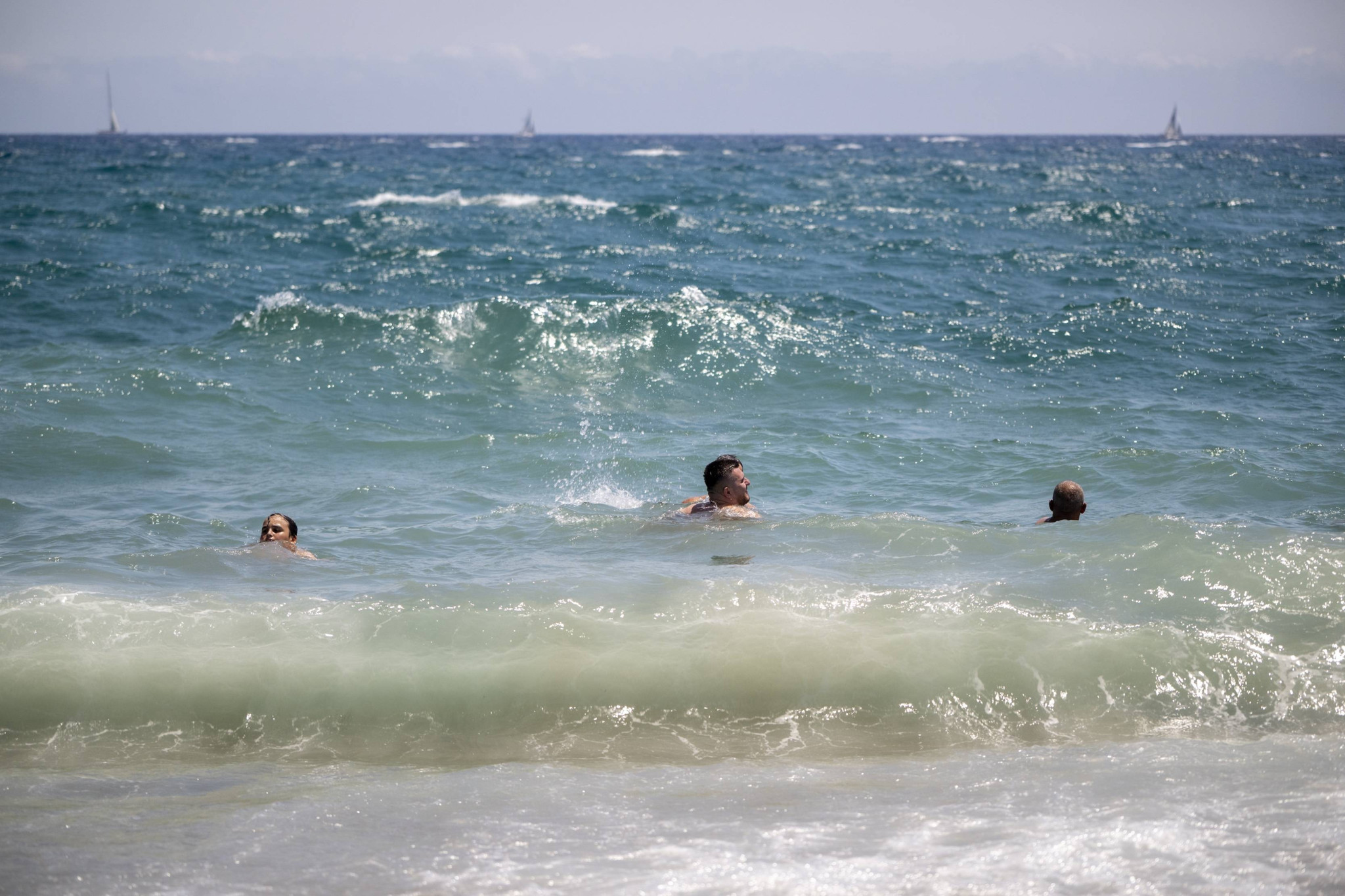 Des baigneurs nagent dans les vagues de la mer Méditerranée à la plage de la Barceloneta, à Barcelone, lors d’une vague de chaleur estivale.