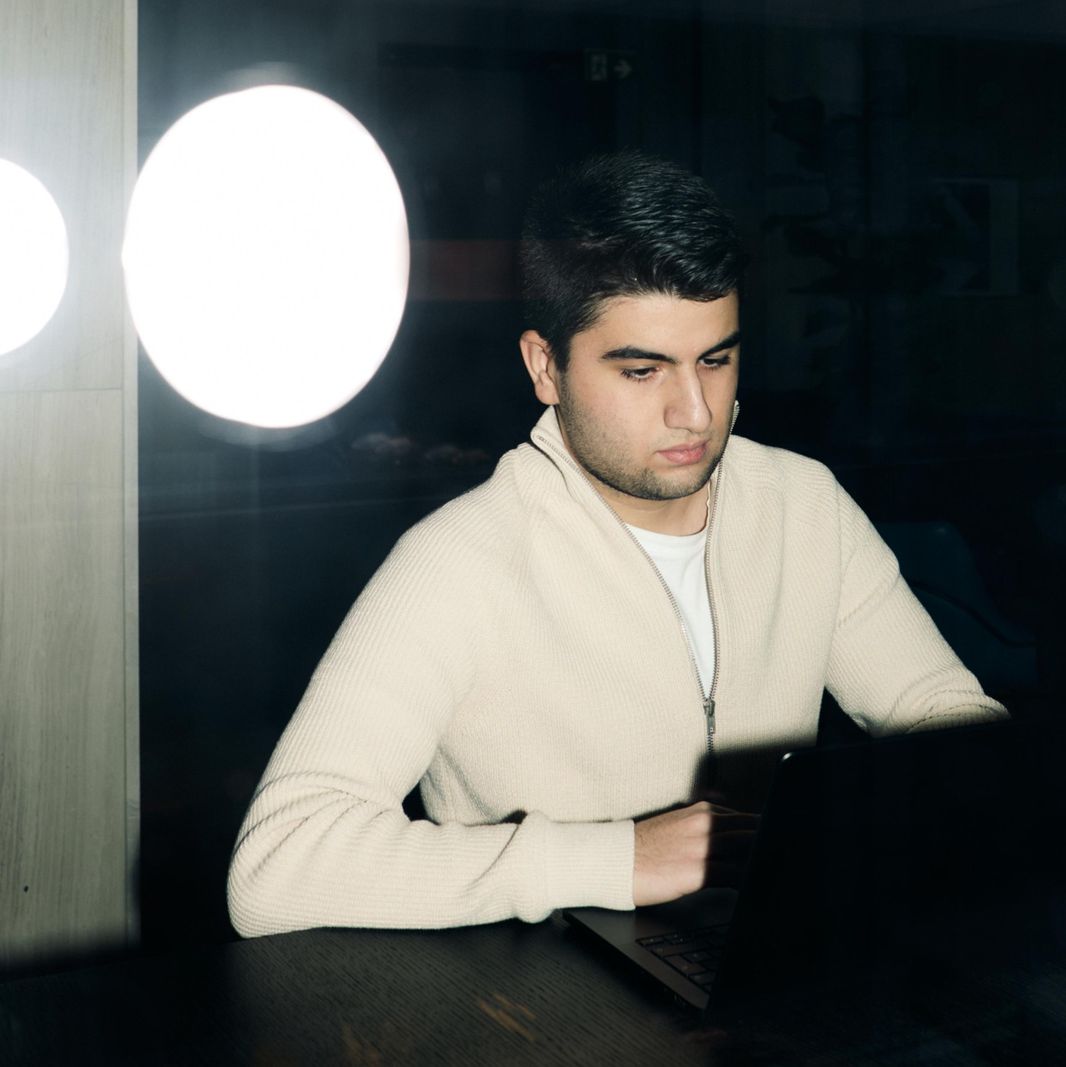 Mann in weissem Pullover arbeitet konzentriert an einem Laptop in einem abgedunkelten Raum.