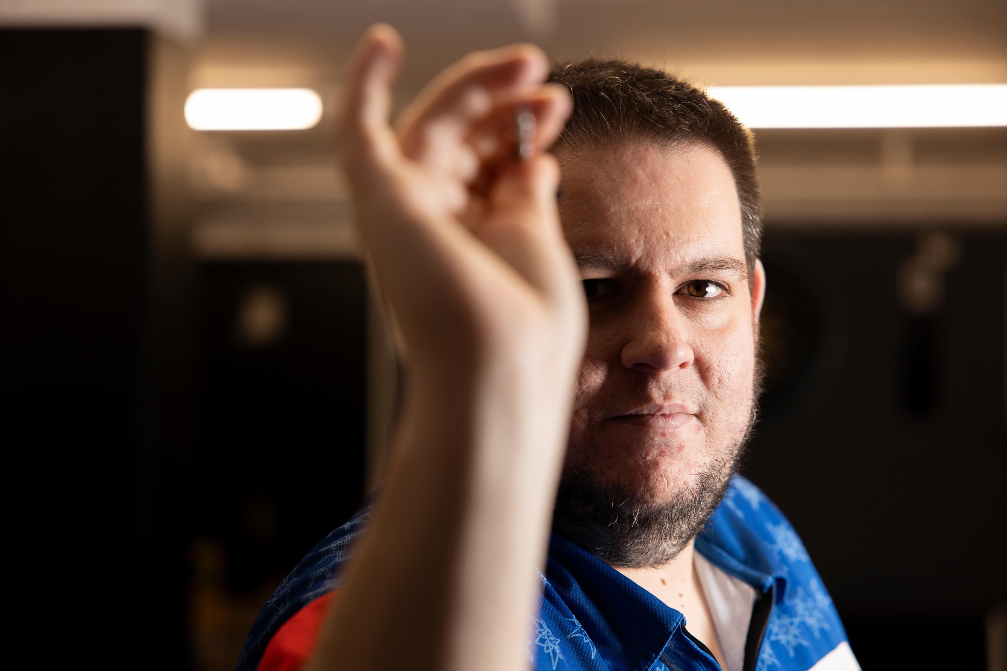 Stefan Bellmont zielt konzentriert mit einem Dartpfeil, gekleidet in einem blau-weissen Hemd, bei der Vorbereitung auf die Dart-WM im Ally Pally.
