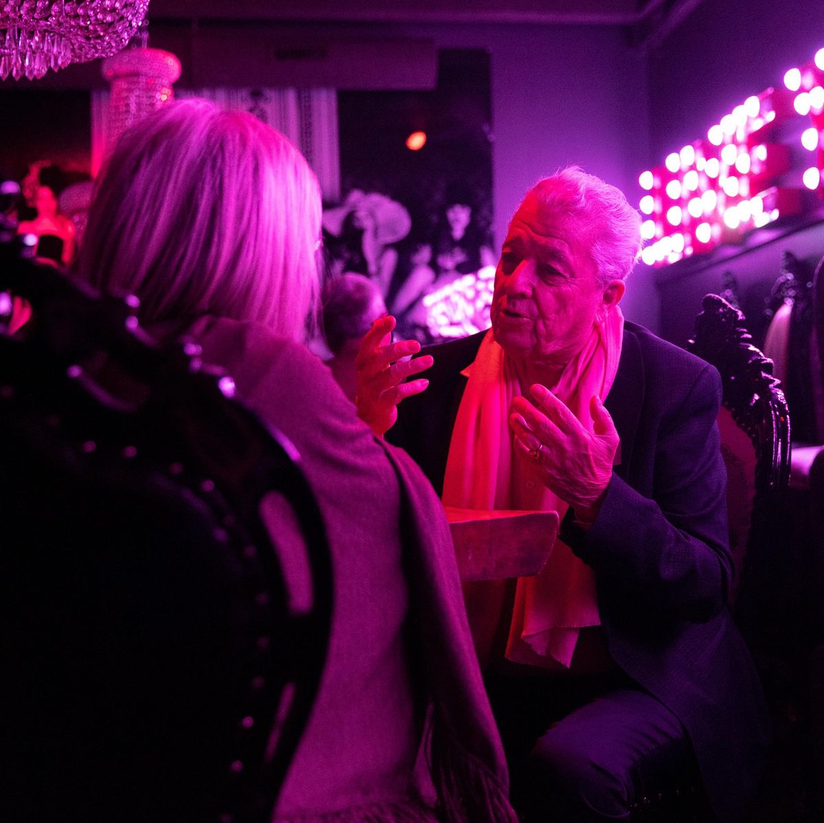 Deux personnes âgées discutent lors d’un speed dating au MAD de Lausanne, sous un éclairage rose vibrant.