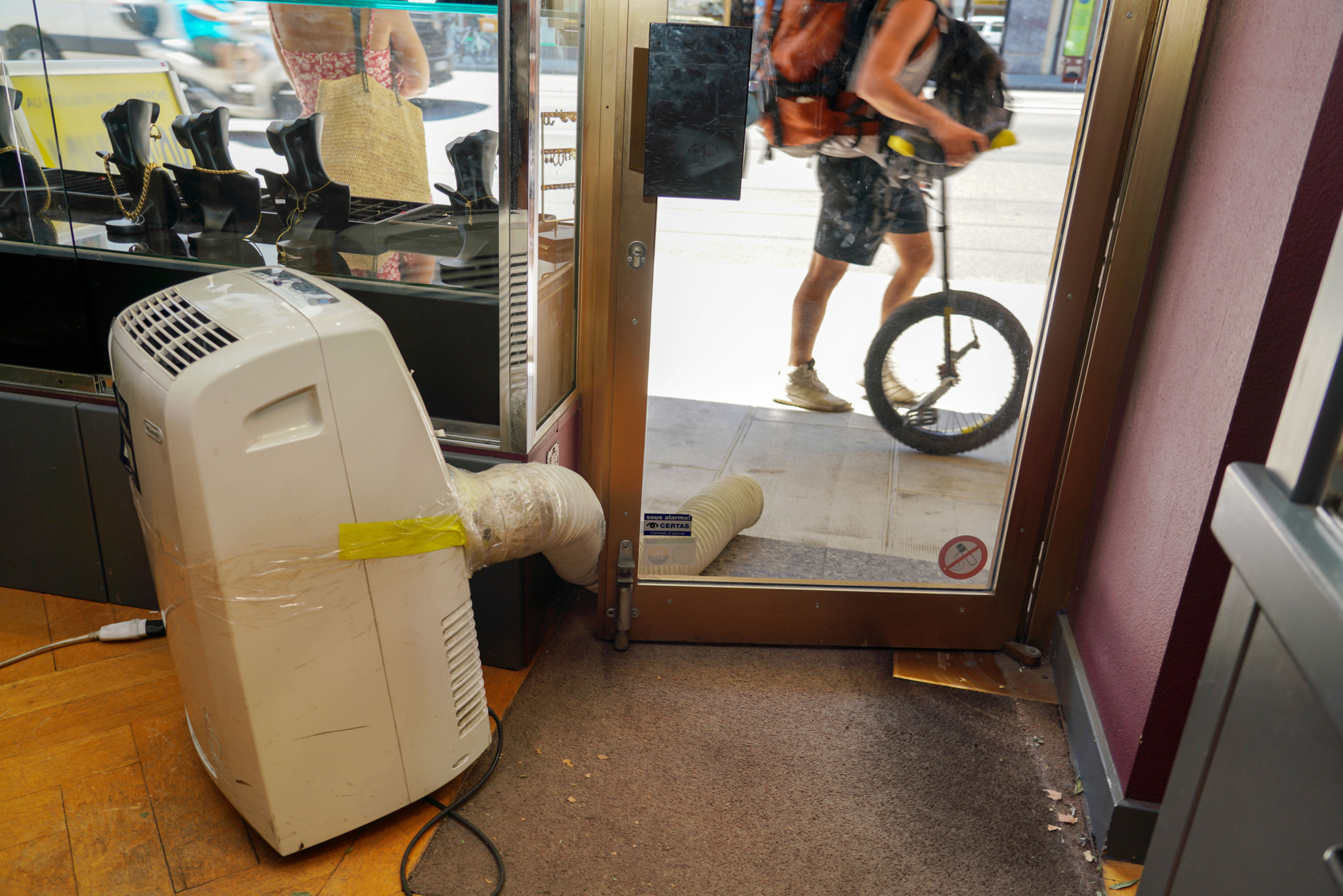Climatiseur mobile installé à l’entrée d’un commerce à Genève, avec un tuyau d’évacuation dirigé vers la porte vitrée ouverte.