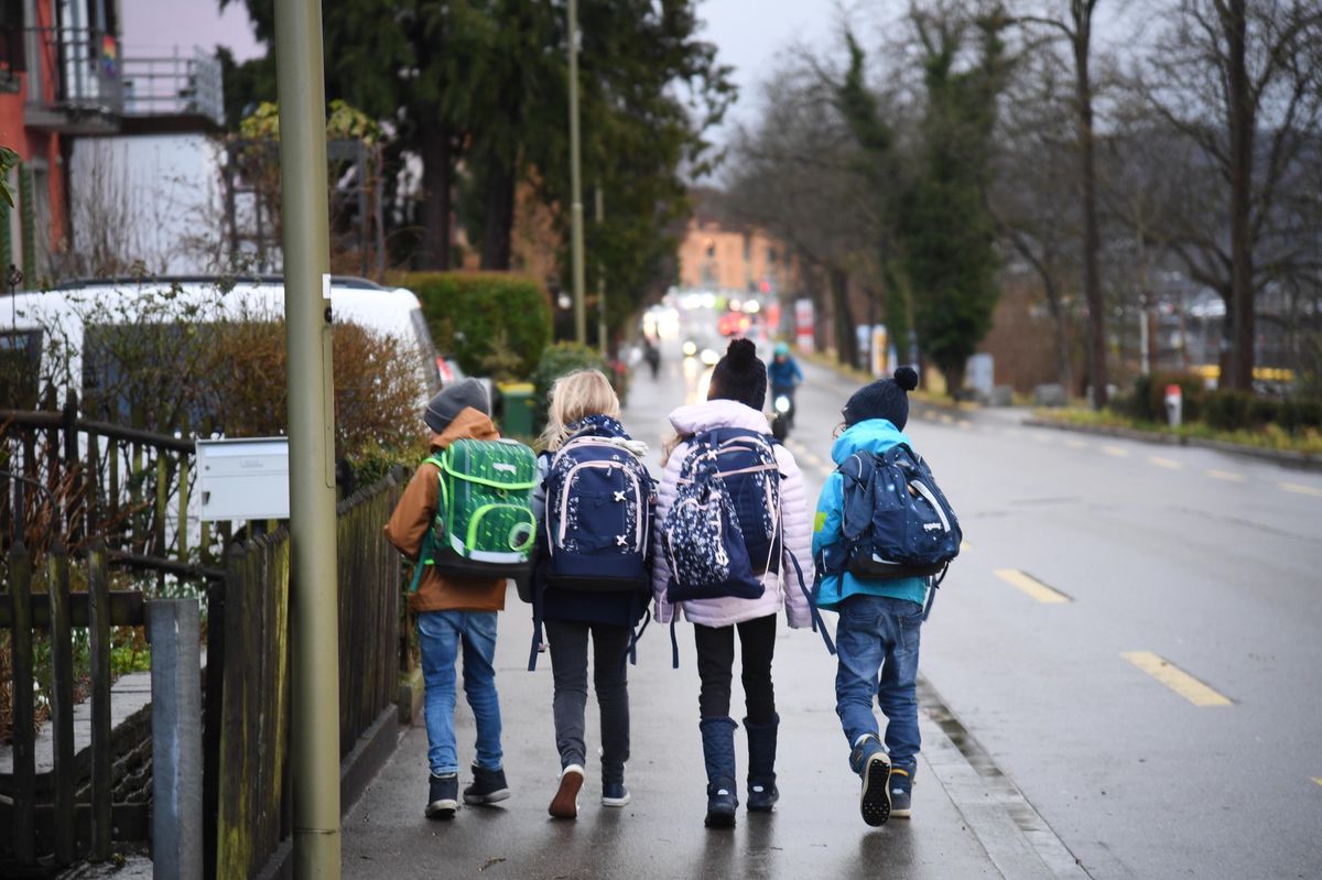Kinder mit Rucksäcken gehen auf der Unteren Vogelsangstrasse zur Schule, begleitet vom Morgenverkehr.