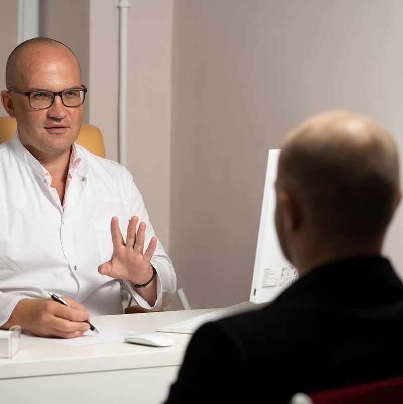 Un médecin en blouse blanche discute avec un patient dans un bureau.