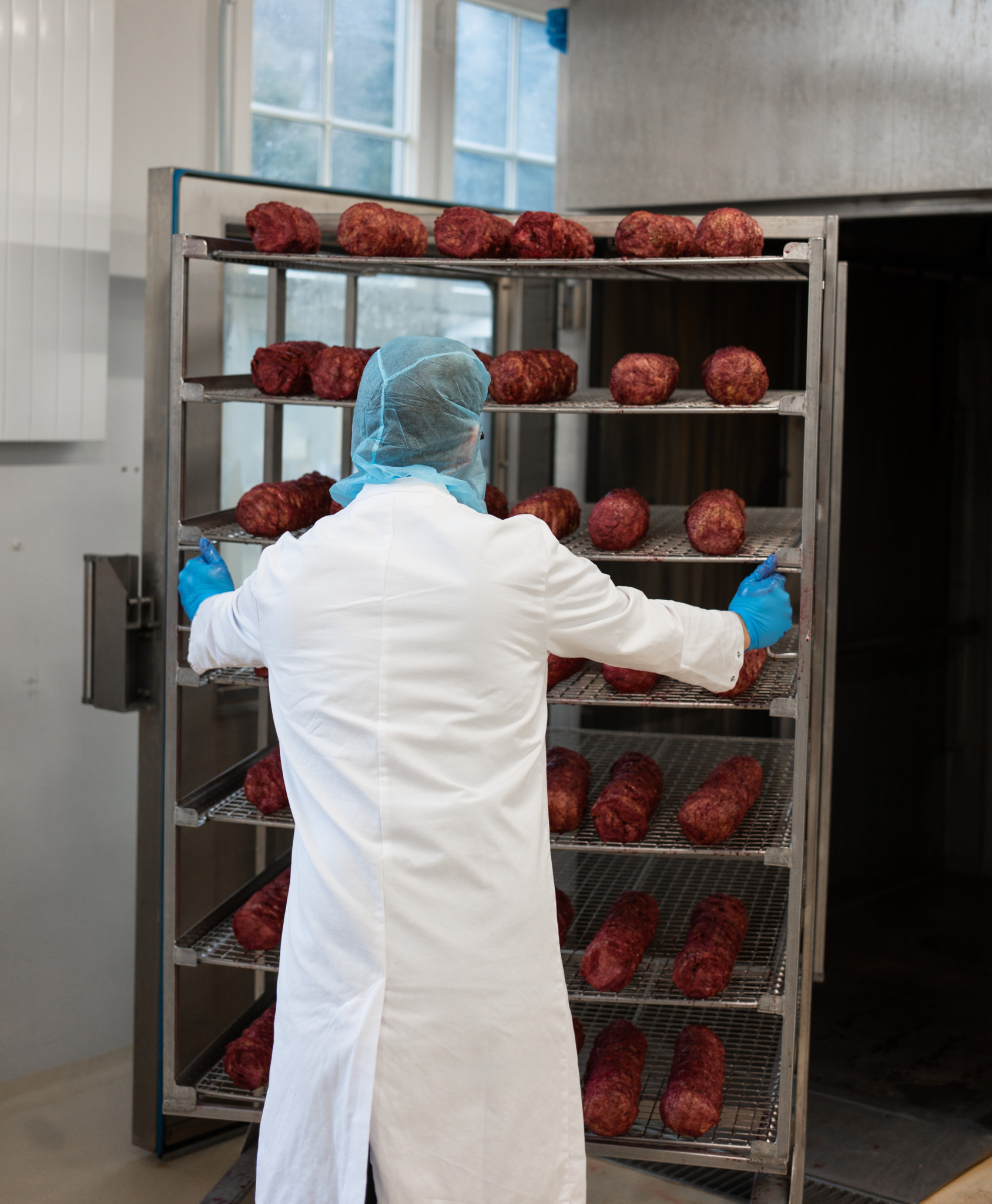 Person in Schutzkleidung platziert Fleischstücke auf einem grossen Metallregal in einer Fabrikumgebung.