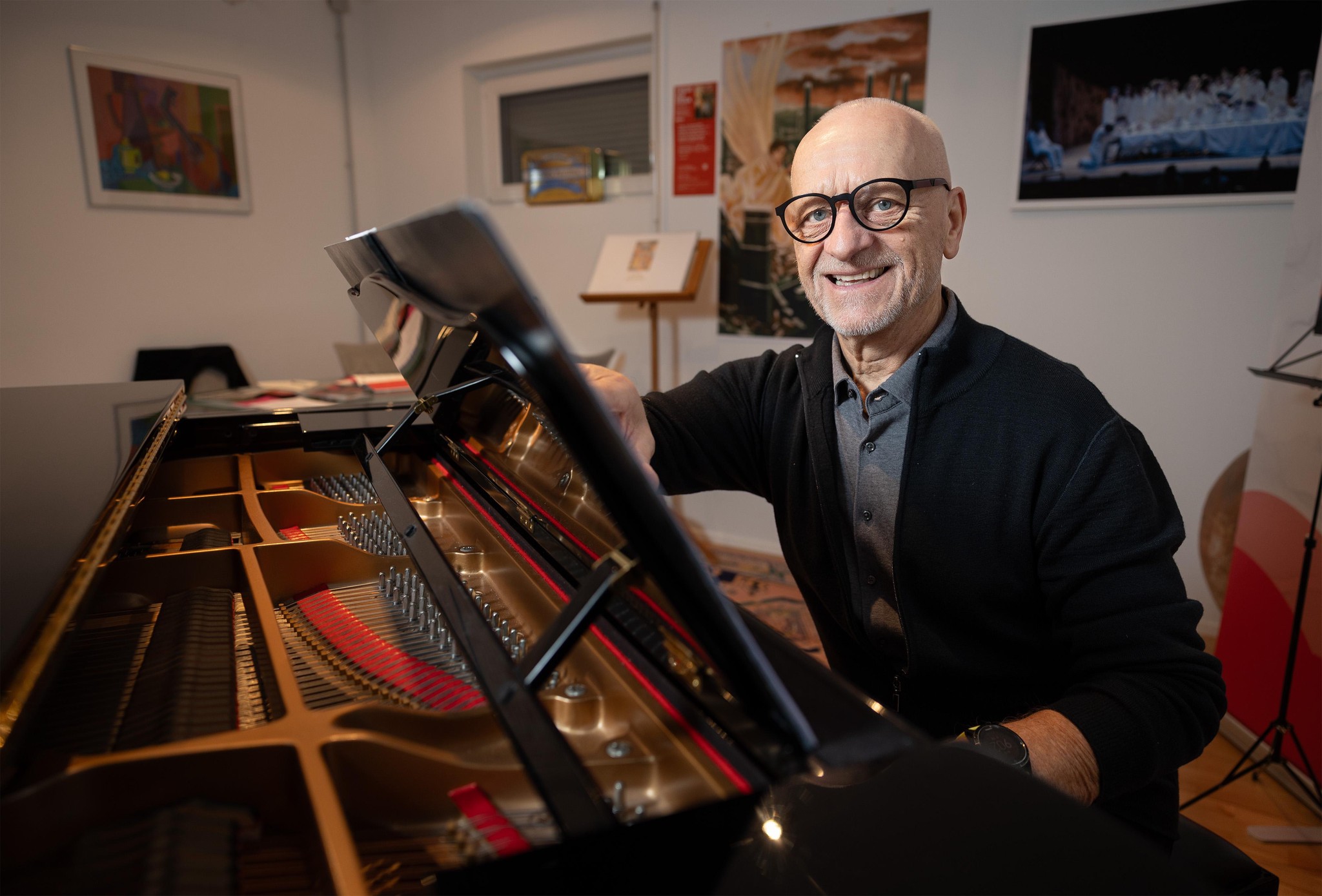 Erich Stoll sitzt lächelnd am Klavier, umgeben von Gemälden und Partituren. Foto von Beat Mathys, Tamedia AG.