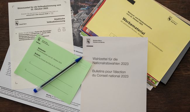 Viele bunte Zettel liegen übereinander. Ganz oben ein grüner und ein blauer Kugelschreiber.