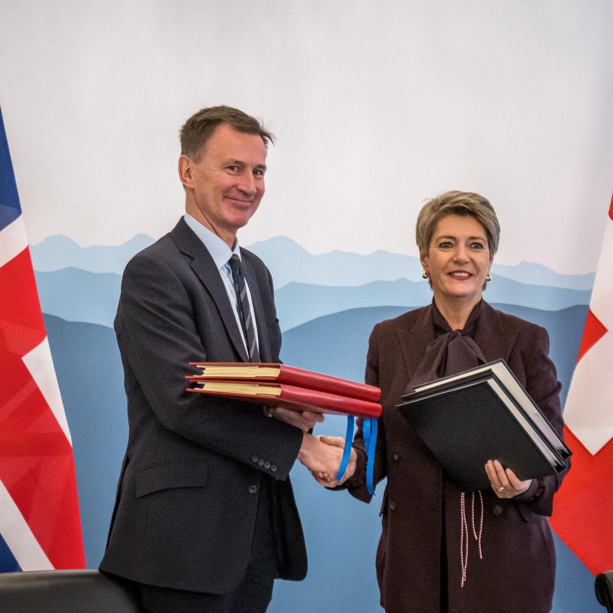 Le chancelier britannique de l’Échiquier, Jeremy Hunt, et la ministre suisse des Finances, Karin Keller-Sutter, se serrent la main après avoir signé un accord sur la reconnaissance mutuelle des services financiers à Berne, le 21 décembre 2023, avec les drapeaux britannique et suisse en arrière-plan.