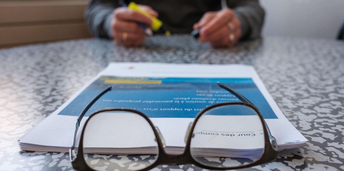 Personne assise à une table avec un rapport de la Cour des comptes sur la protection des mineurs et des lunettes au premier plan.
