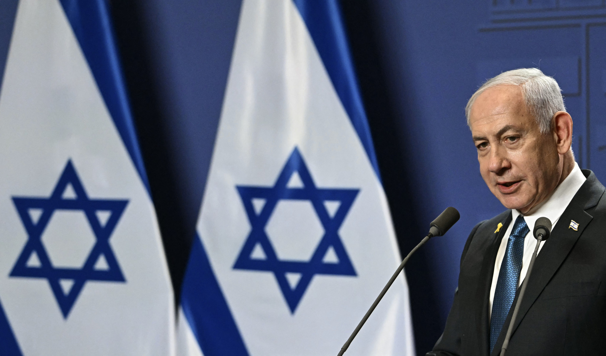 Le Premier ministre israélien Benjamin Netanyahu s’exprime lors d’une conférence de presse à Budapest, le 3 avril 2025, avec des drapeaux israéliens en arrière-plan.