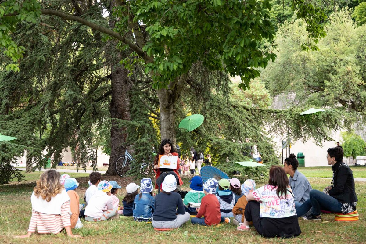 Une personne qui fait la lecture à des enfants assis par terre dans un parc 