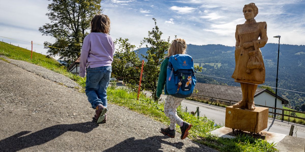 Zwei Kinder wandern den Vreneli-Weg in Guggisberg hinauf. Im Vordergrund die Holzstatue einer Frau. 