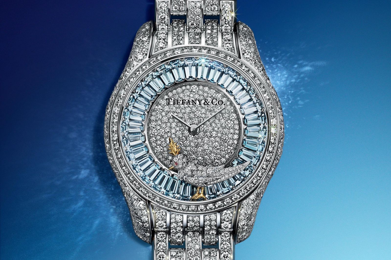 Montre en or blanc incrustée de diamants et saphirs, bracelet en métal poli, cadran étincelant sur fond bleu dégagé.