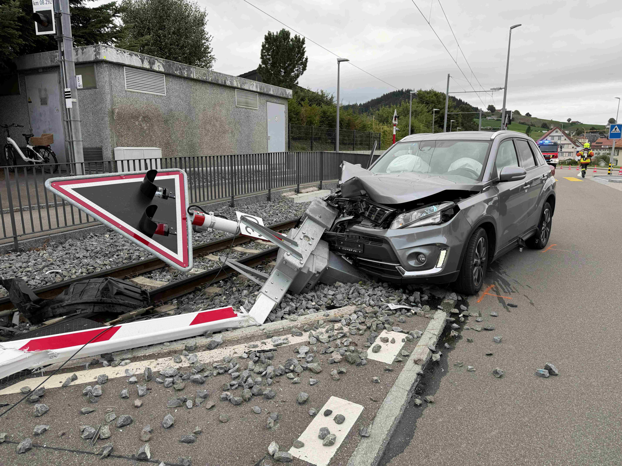 Graues SUV nach Unfall an Bahnübergang mit zerstörter Schranke und umgeknicktem Vorfahrtsschild auf den Gleisen.
