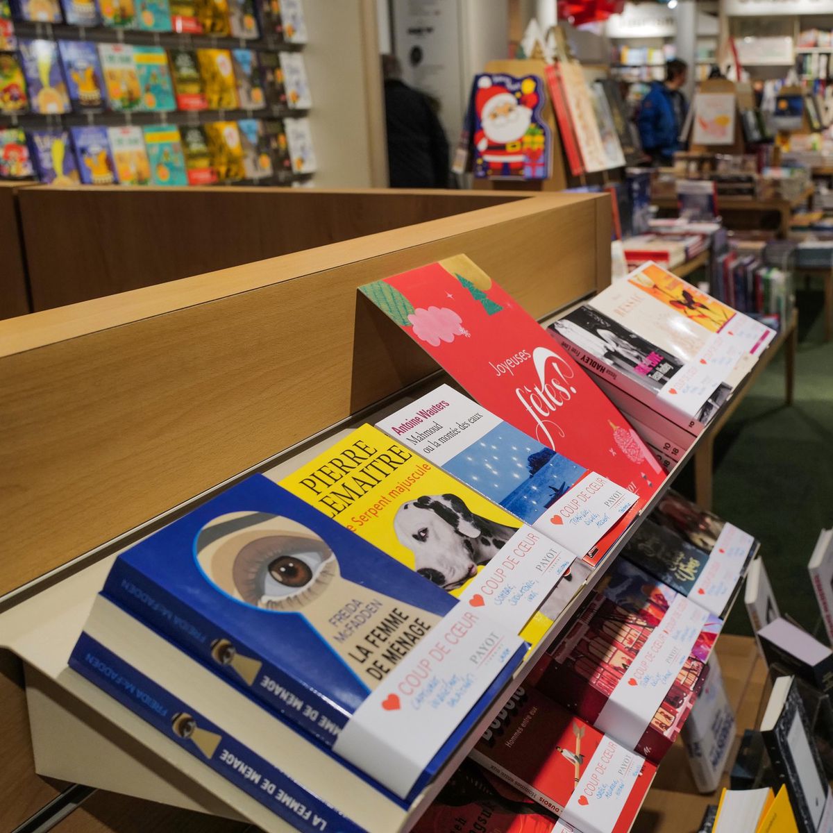 Librairie Payot Genève avec présentoir de livres de poche en avant-plan, organisée par Corinne, avec clients en arrière-plan.