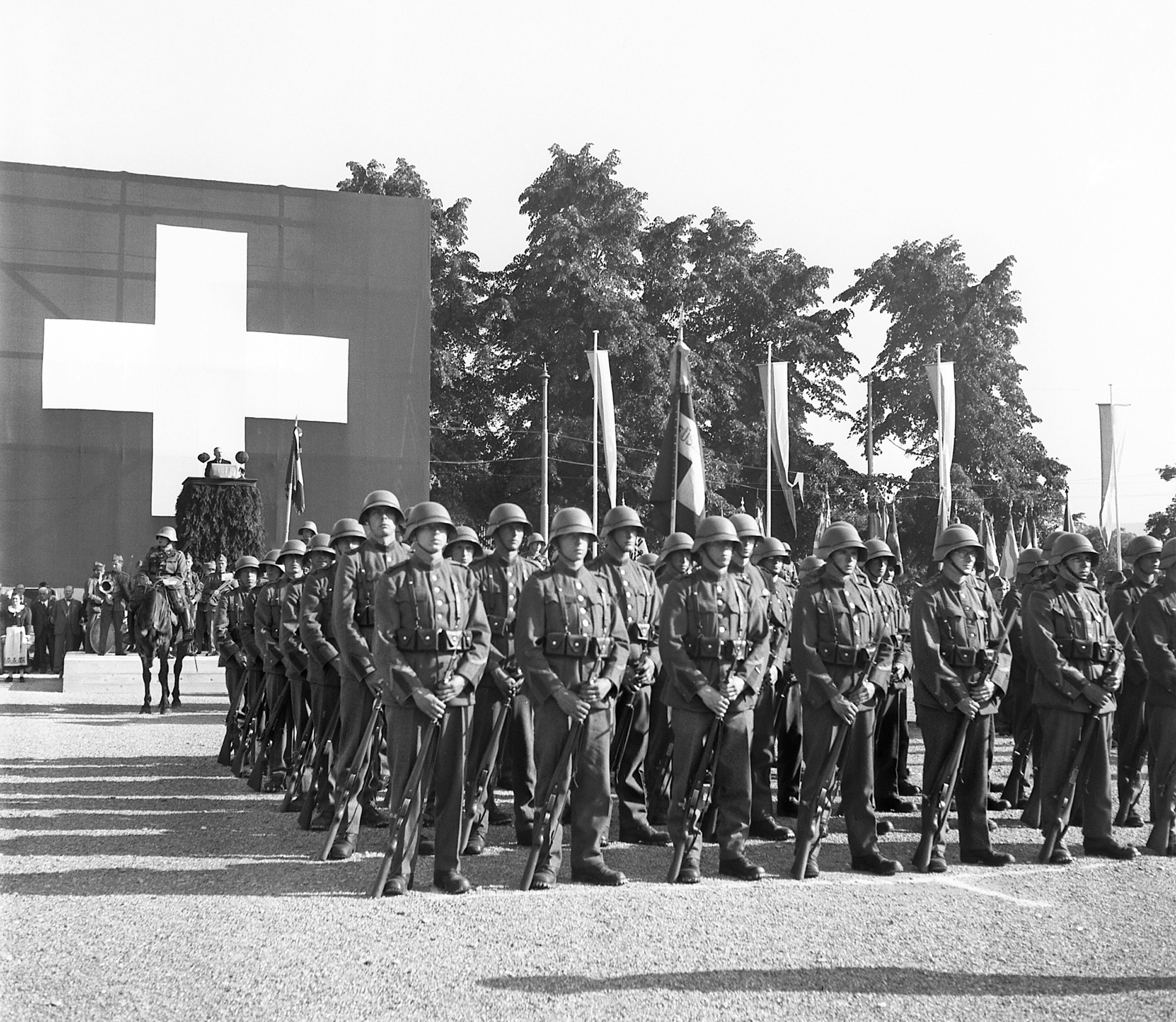 Schweizer Soldaten stehen am 1. August 1940 in Reih und Glied auf dem Tonhalleplatz in Zürich, im Hintergrund eine grosse Schweizer Fahne.
