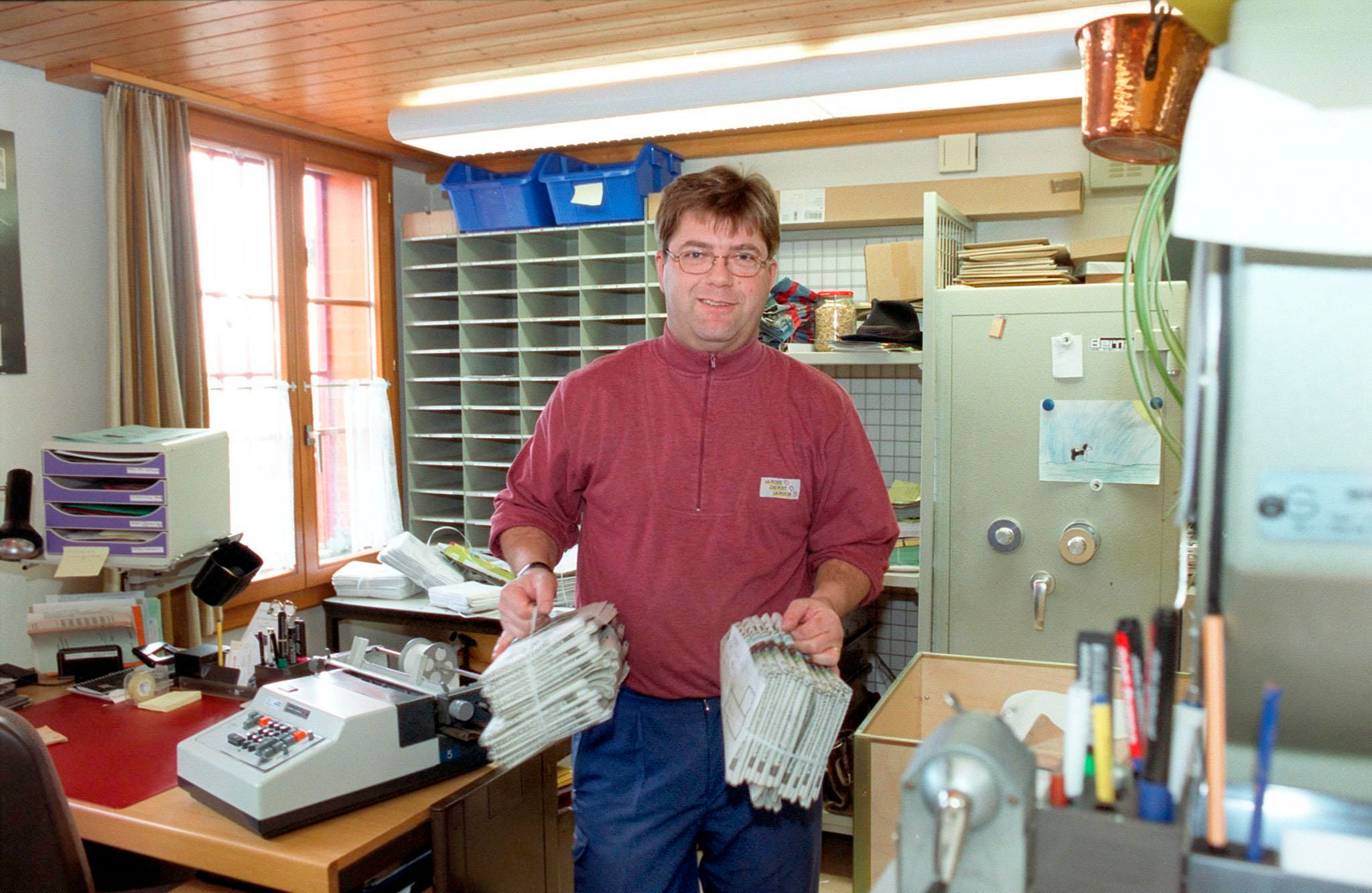 Erich Marti, Posthalter in Hinterfultigen, hält zwei Bündel Post vor seinem Schreibtisch in einem Büro.