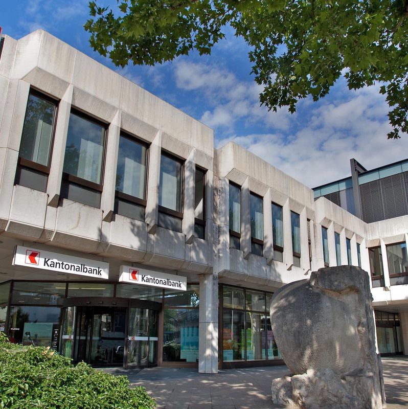 Modernes Gebäude der Basellandschaftlichen Kantonalbank mit Glasfassade und Bäumen im Vordergrund.