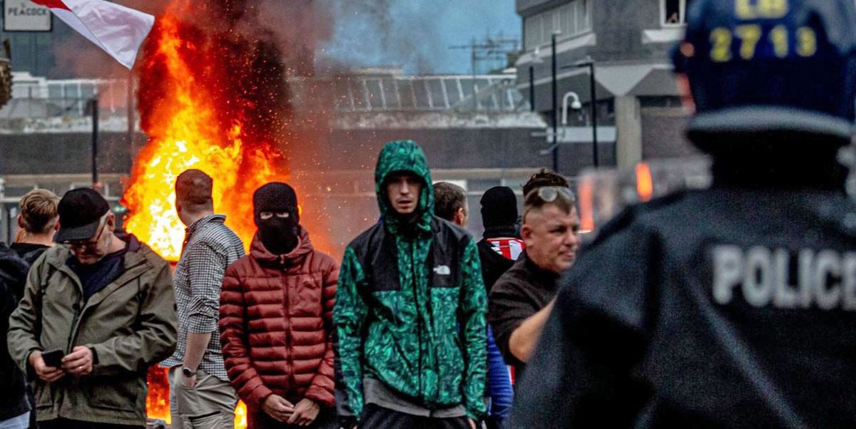 Far-right Aktivisten halten eine 'Enough is Enough'-Demonstration in Sunderland, England, ab. Im Hintergrund brennt ein grosses Feuer und es gibt Rauch. Einige Personen tragen britische Flaggen, während Polizisten die Szene überwachen.