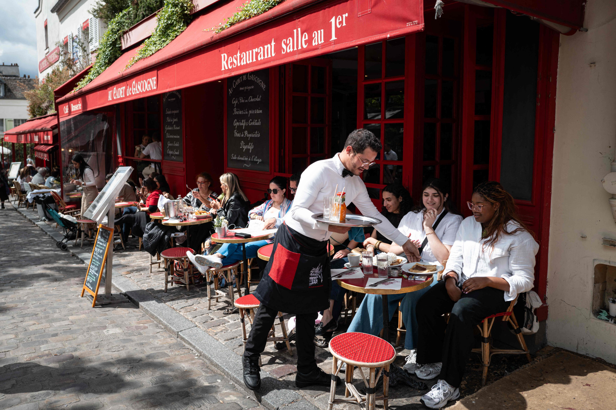 Customers sit on the terrasse of a restaurant at Place du Tertre, the famous painters' square on the hill in the Montmartre district, northern Paris, on May 21, 2024. On the Place du Tertre, artists  but there is no rush of tourists and the restaurant terraces are rather empty, just a few days before the 2024 Paris Olympics Games. (Photo by Miguel MEDINA / AFP)