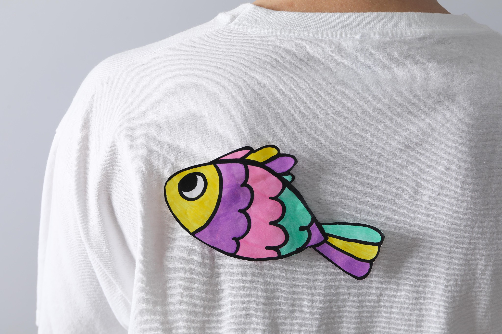 Poisson coloré en papier attaché au dos d’un t-shirt blanc pour le 1ᵉʳ avril.