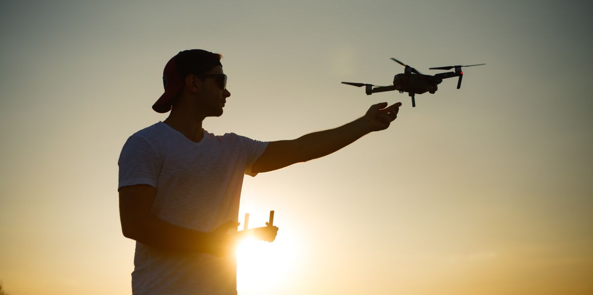 Homme contrôlant un drone avec une télécommande au coucher du soleil.