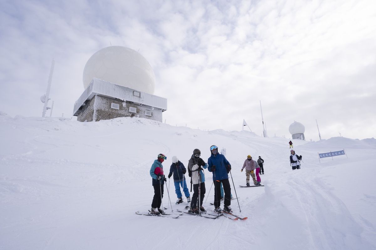 Groupe de skieurs sur une piste enneigée à Les Dappes, domaine skiable de la Dôle, avec des bâtiments radar en arrière-plan, le 10 janvier 2024, lors de l'ouverture des pistes du domaine skiable franco-suisse autour du massif de la Dôle.