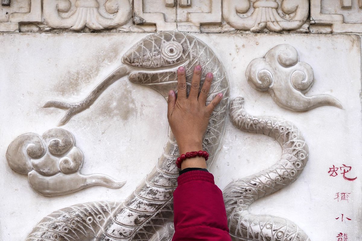 Une femme touche une figure de serpent sur un mur en pierre au temple taoïste Baiyun à Pékin, avant le Nouvel An lunaire chinois de 2025.