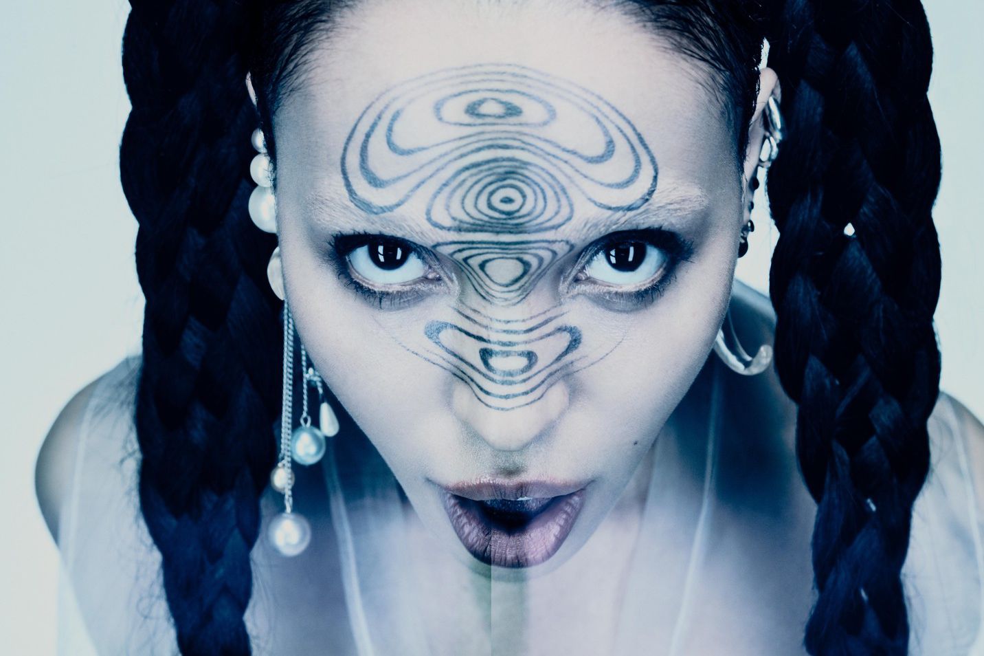 Femme avec des tresses épaisses et un motif artistique sur le front, regard intense vers la caméra.