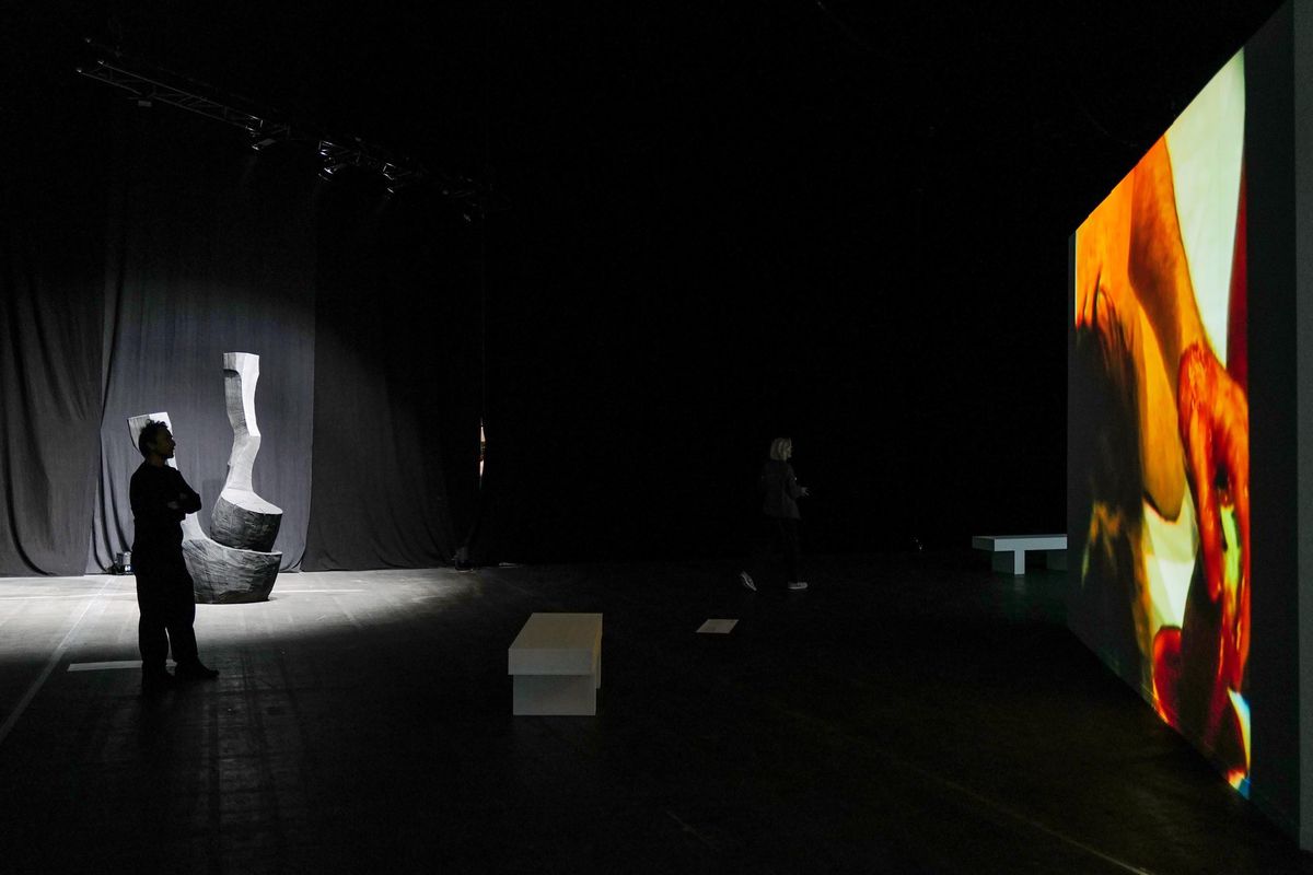 Exposition d’art à Genève avec une sculpture sur un socle et une grande projection lumineuse sur un écran, dans une salle sombre à Palexpo.