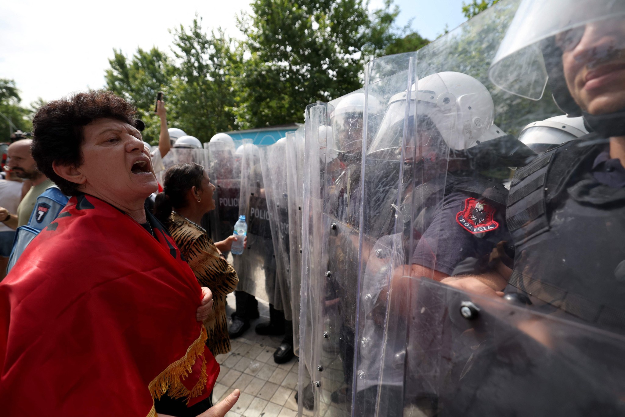 Demonstrantin in rotem Umhang konfrontiert Polizei-Sondereinsatzkräfte vor dem Parlament in Tirana bei Protest gegen Trump-Luxusresort in Albanien.