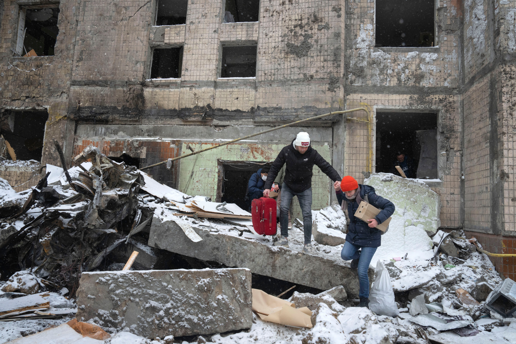 People walk with belongings out from an apartment building destroyed after Tuesday's Russian attack in Kyiv, Ukraine, Wednesday, Jan. 3, 2024. (AP Photo/Efrem Lukatsky)