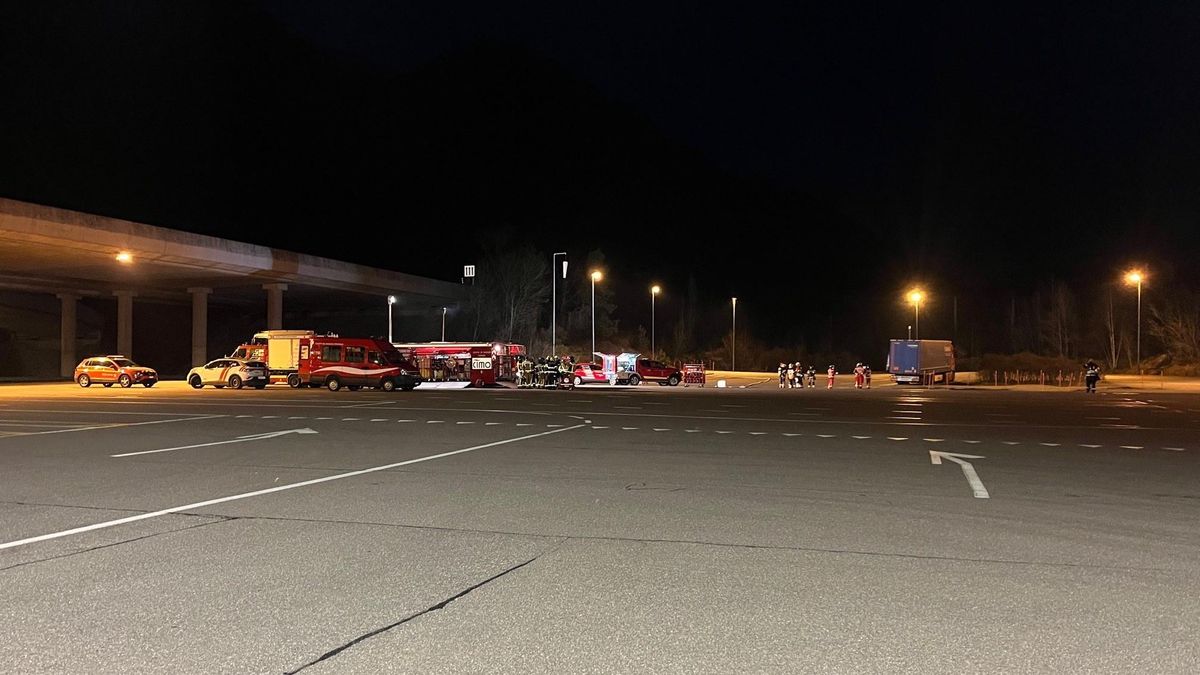 Intervention nocturne des services d’urgence sur une aire de stationnement, avec plusieurs véhicules de secours et camions illuminés sous les lampadaires.