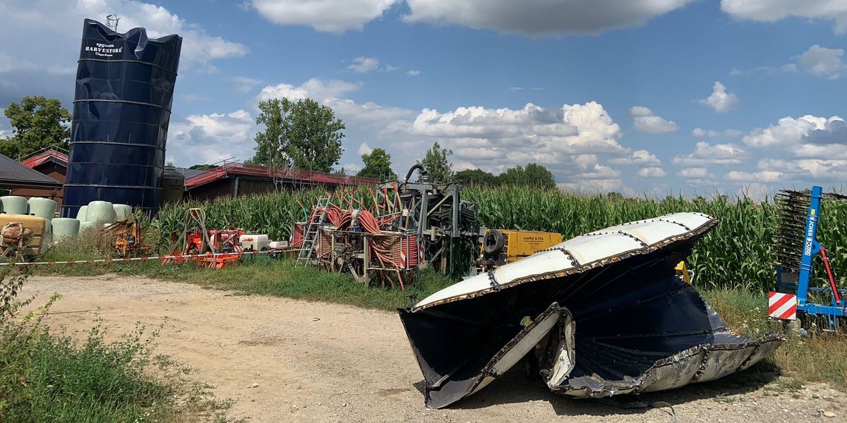 Silo endommagé par une tornade sur une ferme avec du matériel agricole sous un ciel partiellement nuageux.