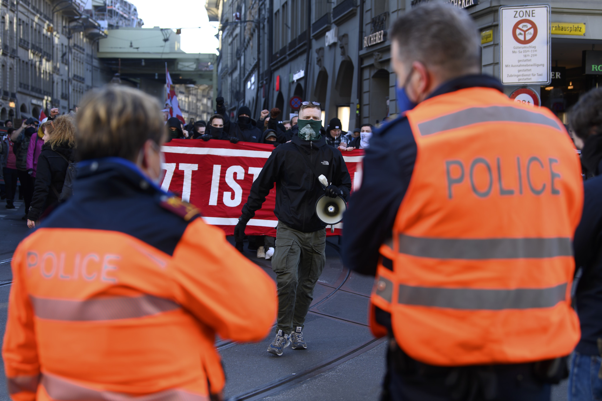 Polizisten beobachten Demonstranten mit rotem Banner gegen Corona-Massnahmen in Bern, Januar 2022. Ein Teilnehmer trägt Halstuch der rechtsextremen «Jungen Tat».