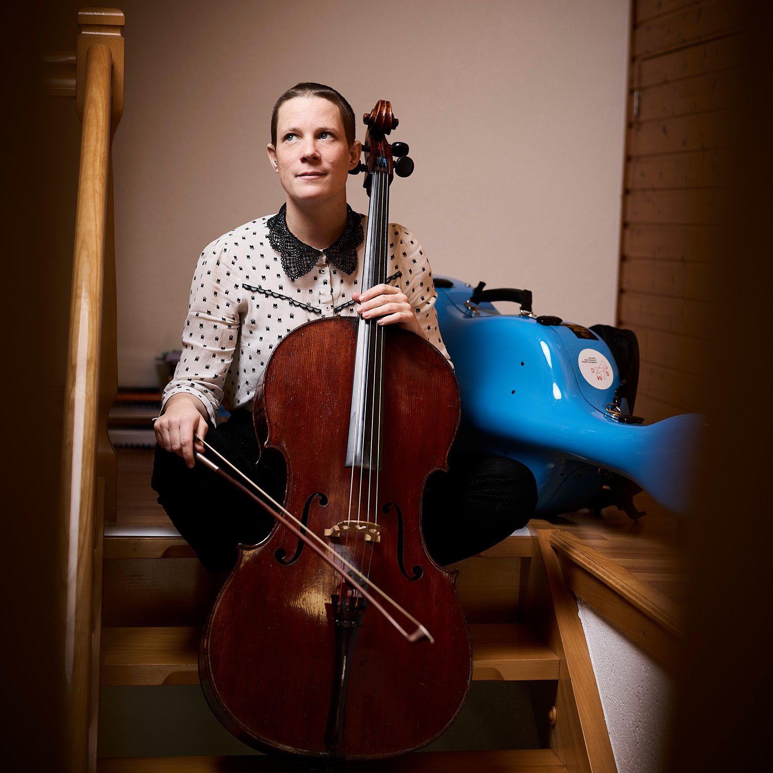 La violoncelliste Elsa Dorbath assise sur des escaliers avec son violoncelle, fondatrice de l’ensemble Camerata Ataremac à Ollon-la-Ville, le 17 janvier 2025.