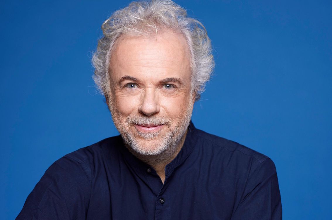 Portrait de Frédéric Lenoir en chemise noire et jeans, sur fond bleu, pris par Pascal Ito. Mention obligatoire incluse en bas de l’image.