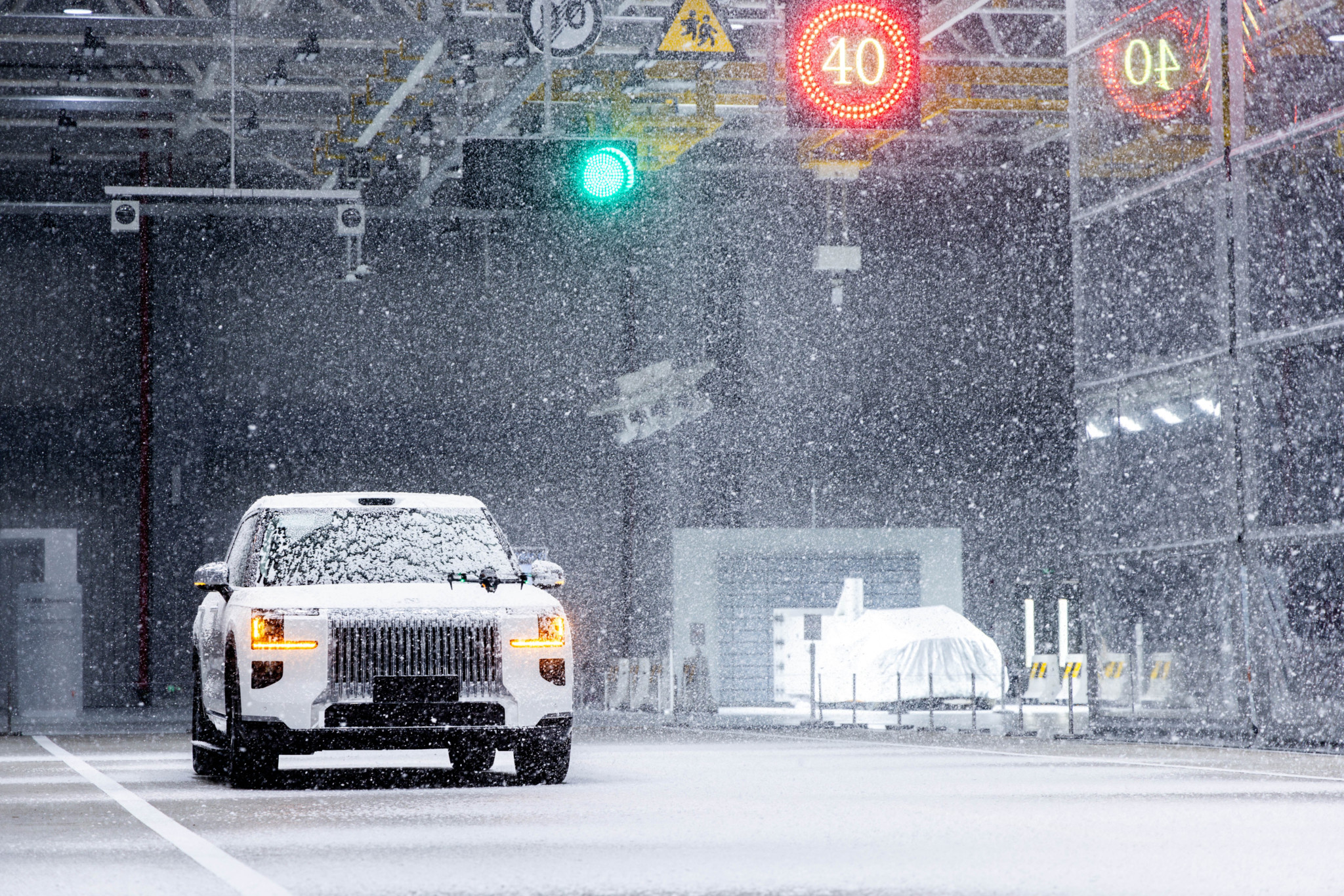 Ein schneebedecktes ECRI-Testfahrzeug (Geely-Tochter) fährt bei starkem Schneefall unter einer Ampel mit Tempolimit 40.