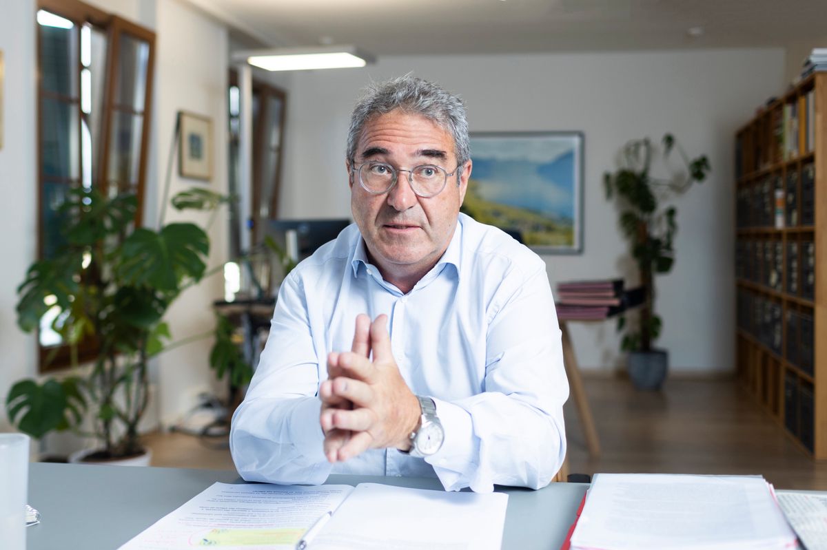 Homme en chemise blanche assis à un bureau dans un bureau lumineux, avec des plantes en arrière-plan.