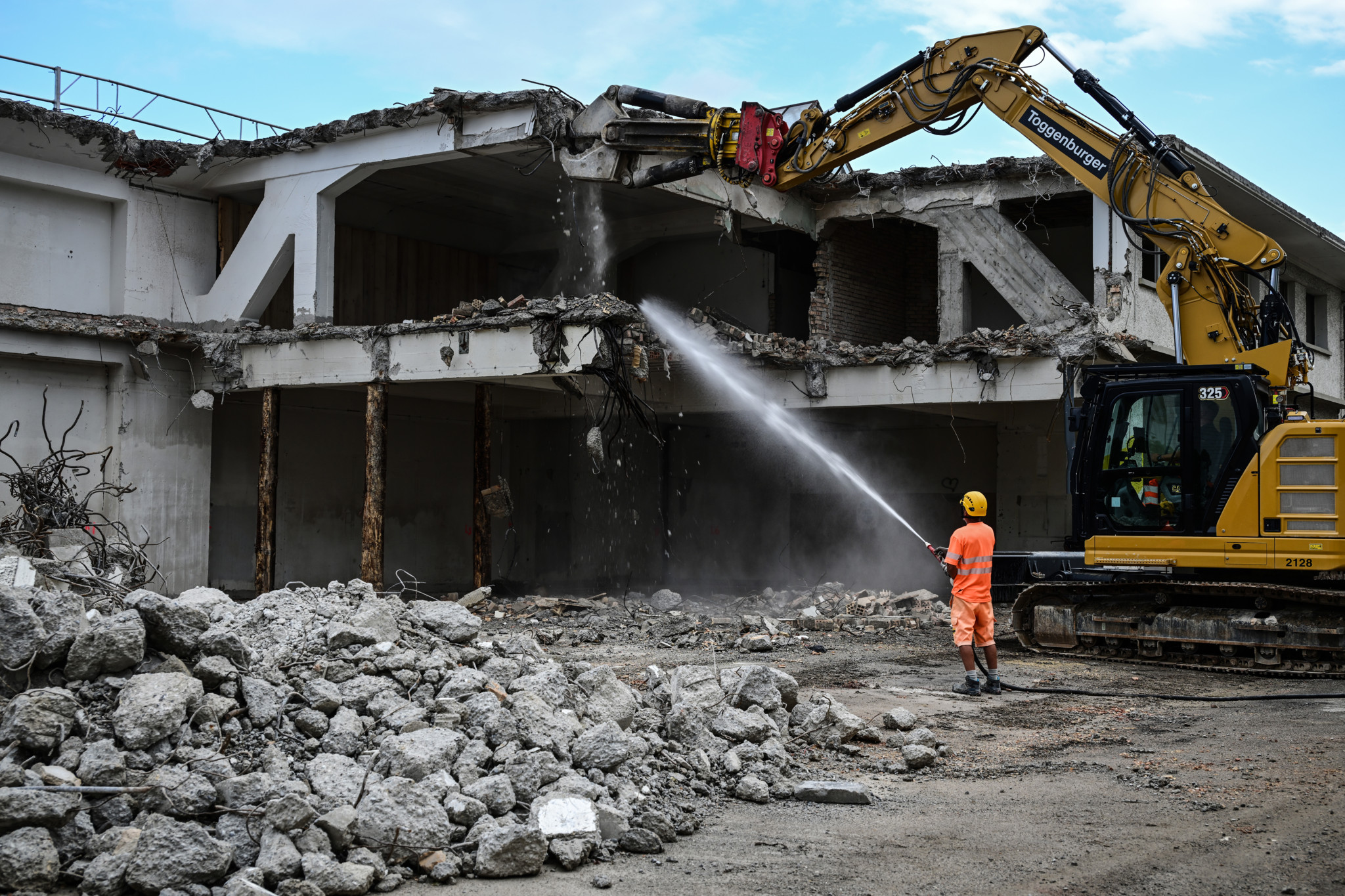 Abriss des alten Busdepots in Winterthur: Arbeiter mit Wasserschlauch neben gelbem Bagger vor teilweise zerstörtem Gebäude.