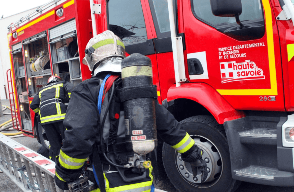 Pompiers de Haute-Savoie en tenue complète, prêts à intervenir près d'un camion de secours rouge avec des équipements de lutte contre l'incendie.