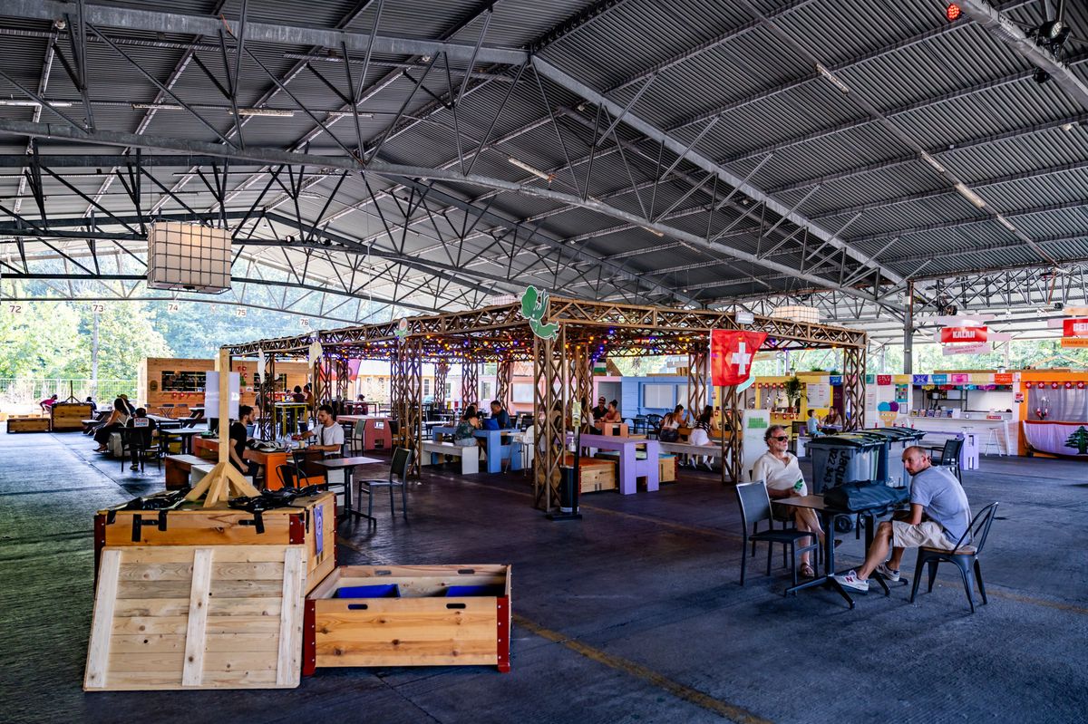 Salle de grande taille des Halles de la Jonction abritant un food court diverse avec des stands de différentes cuisines et des personnes assises à des tables. Photo Pierre Albouy/Tribune de Genève.