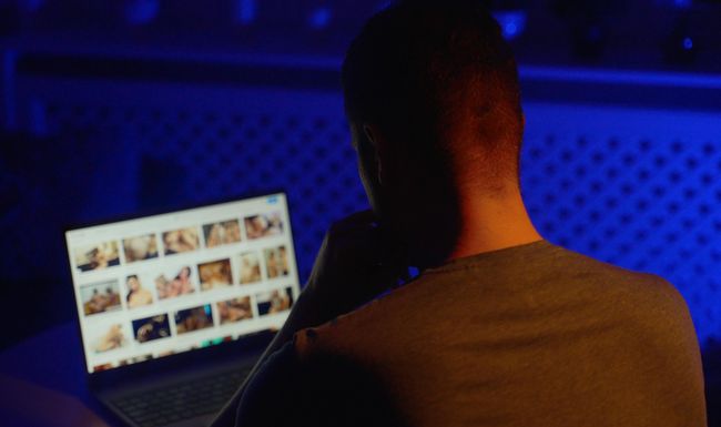 Mann von hinten, schaut Nacktbilder an einem Computer an.