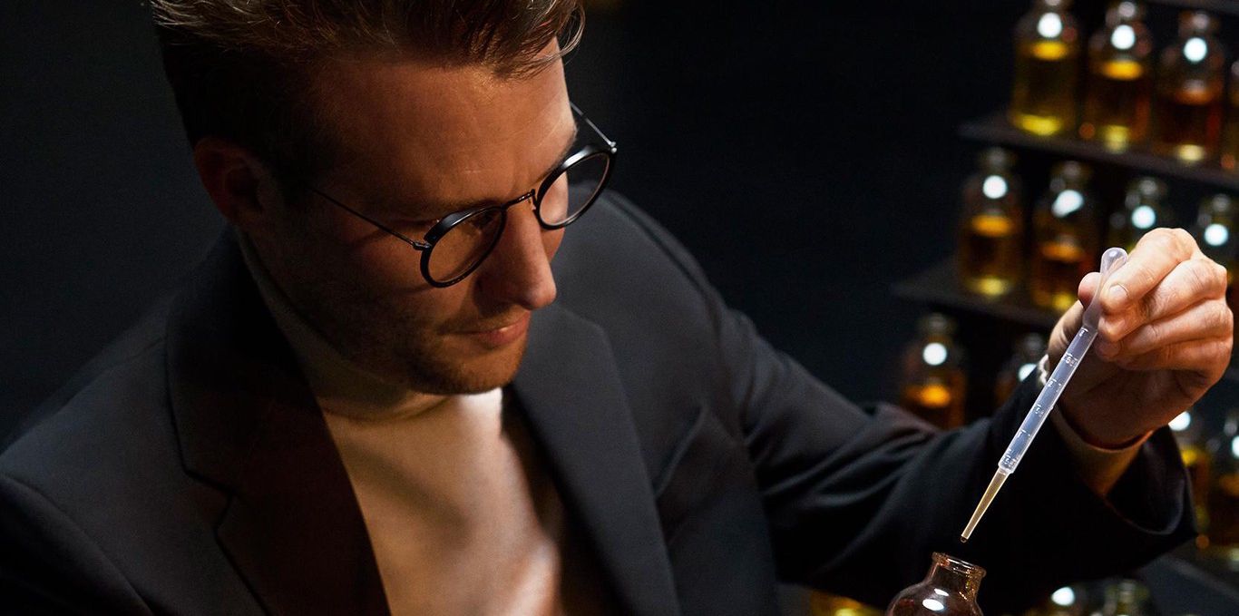 Un homme en costume utilise une pipette pour tester des flacons de parfum alignés sur une table.