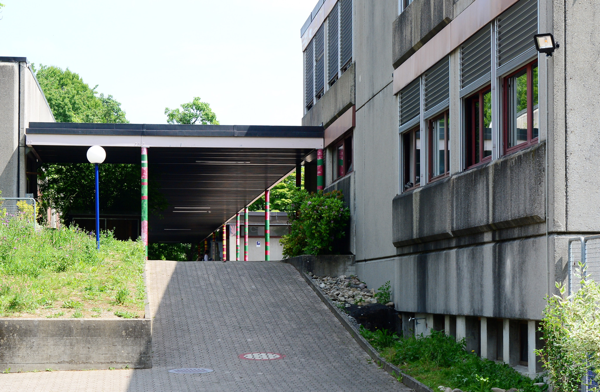 Ansicht des Schulhauses Stenacker in Winterthur mit einem überdachten Weg und farbigen Säulen. Foto vom 02.06.2022.