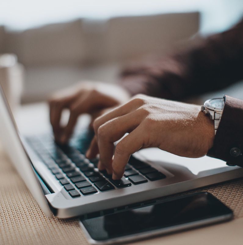 Mains tapant sur un ordinateur portable avec une montre visible au poignet.